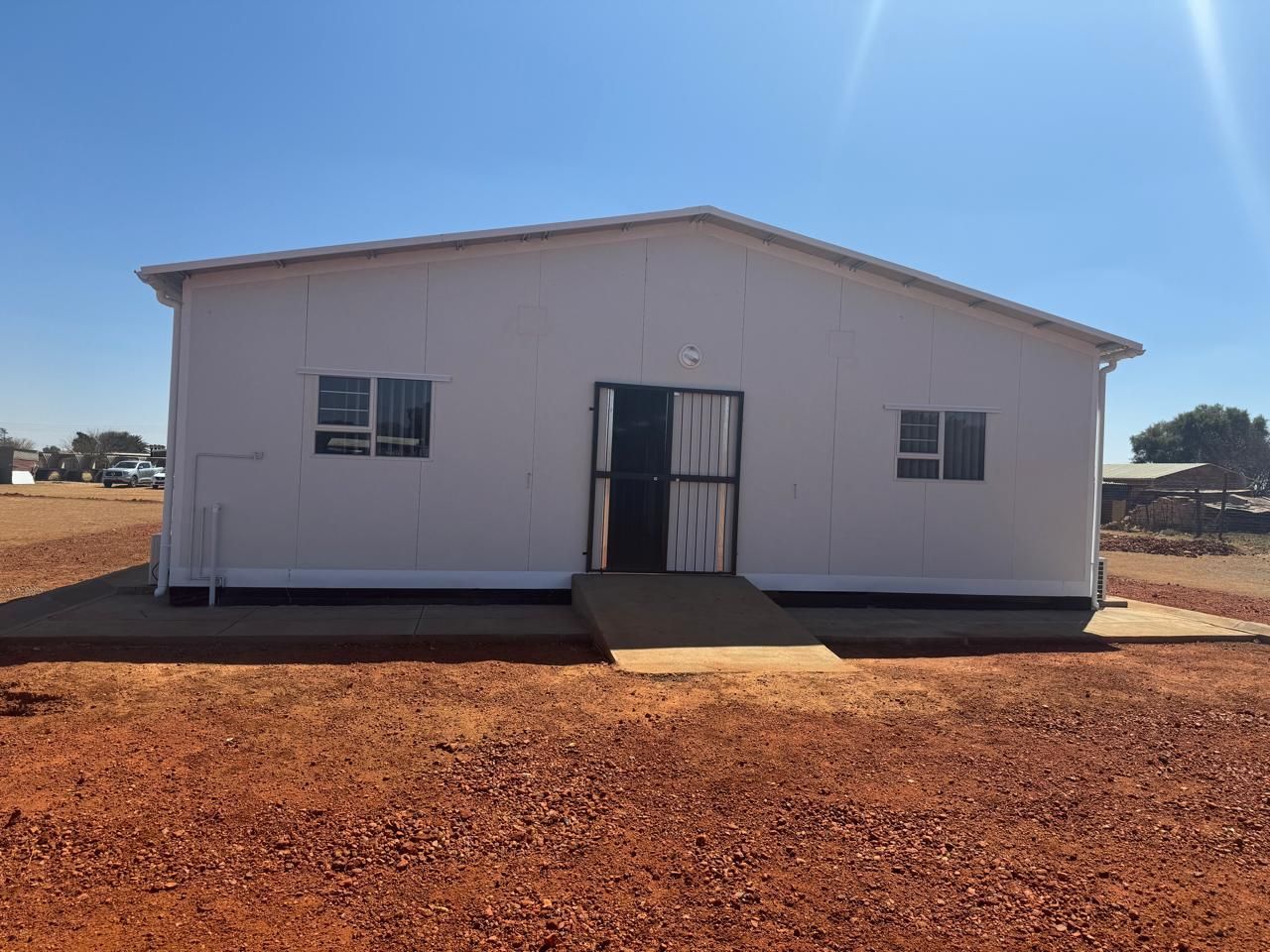 A white house is sitting in the middle of a dirt field.