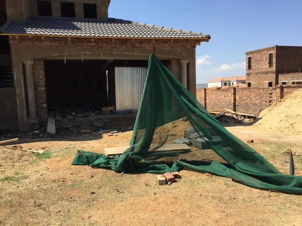 A green tarp is laying on the ground in front of a house under construction.