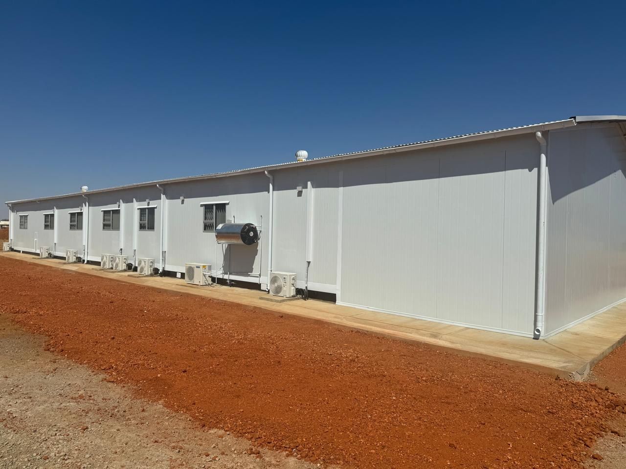A large white building is sitting on top of a dirt field.