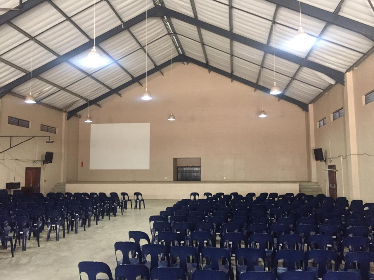A large auditorium with blue chairs and a projector screen