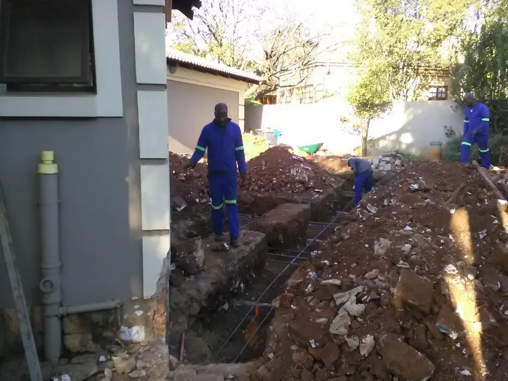 A group of construction workers are digging a hole in the ground in front of a house.