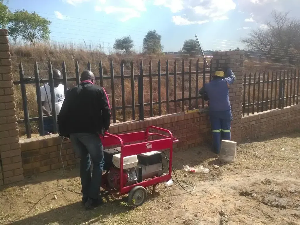A man is standing next to a red generator in front of a fence.