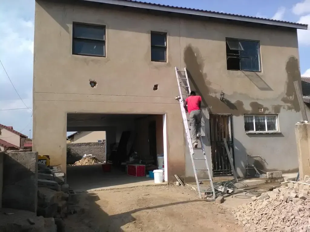 A man on a ladder paints the side of a house