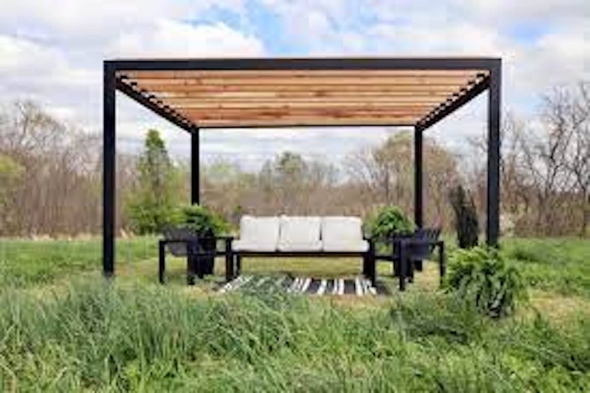 A pergola with a couch and chairs underneath it in a grassy field.