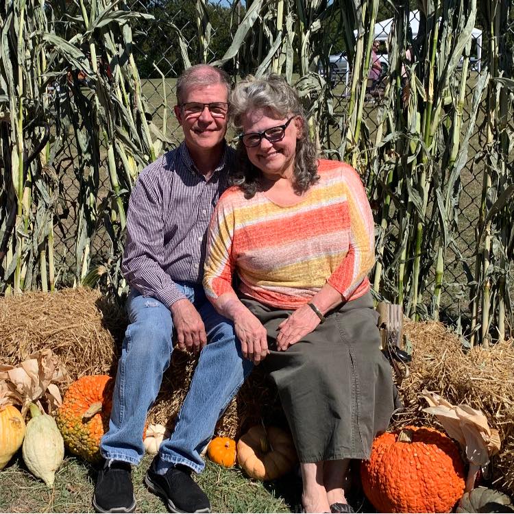 A man and a woman are sitting on hay bales in front of pumpkins.
