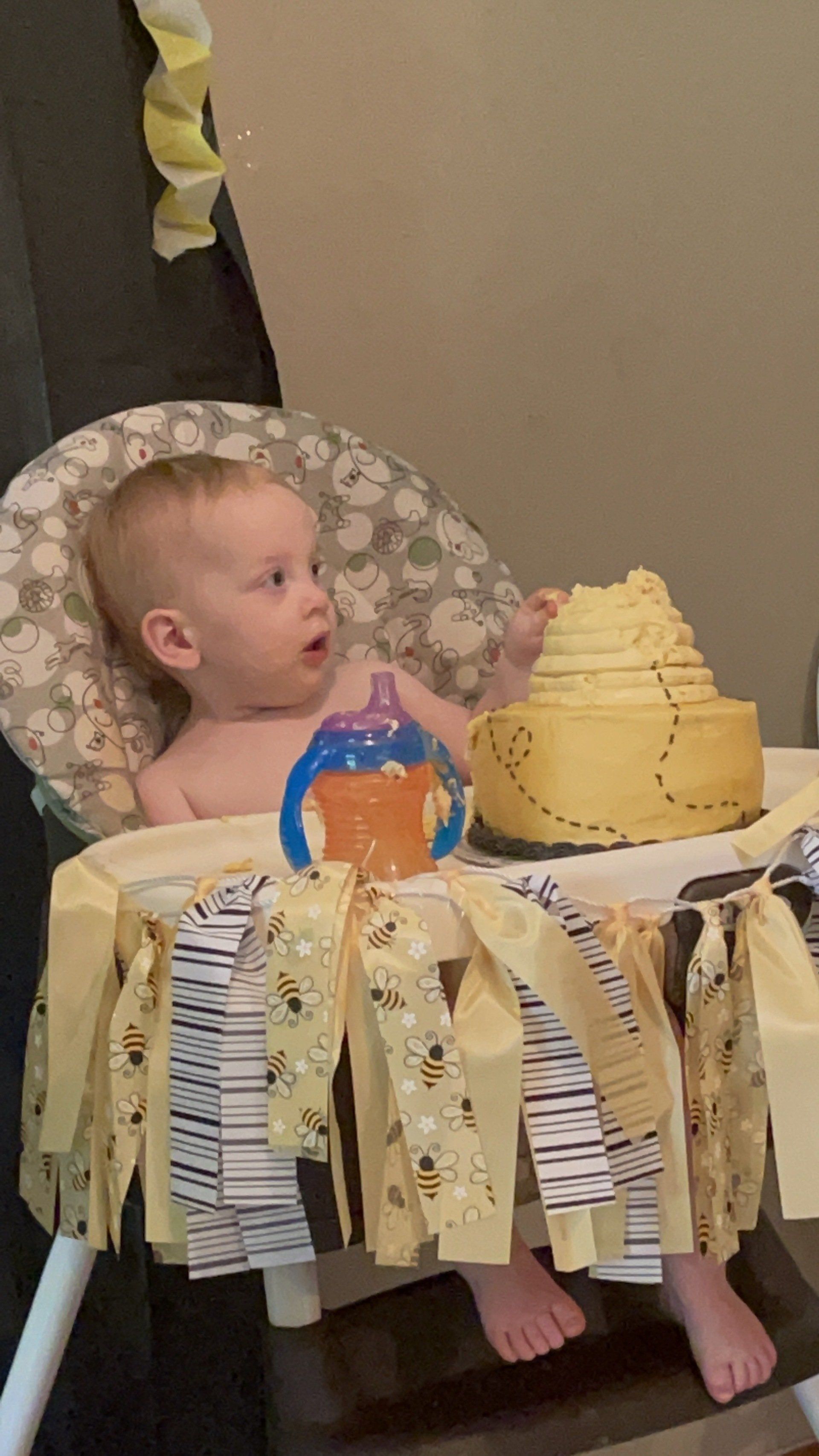A baby is sitting in a high chair next to a cake.
