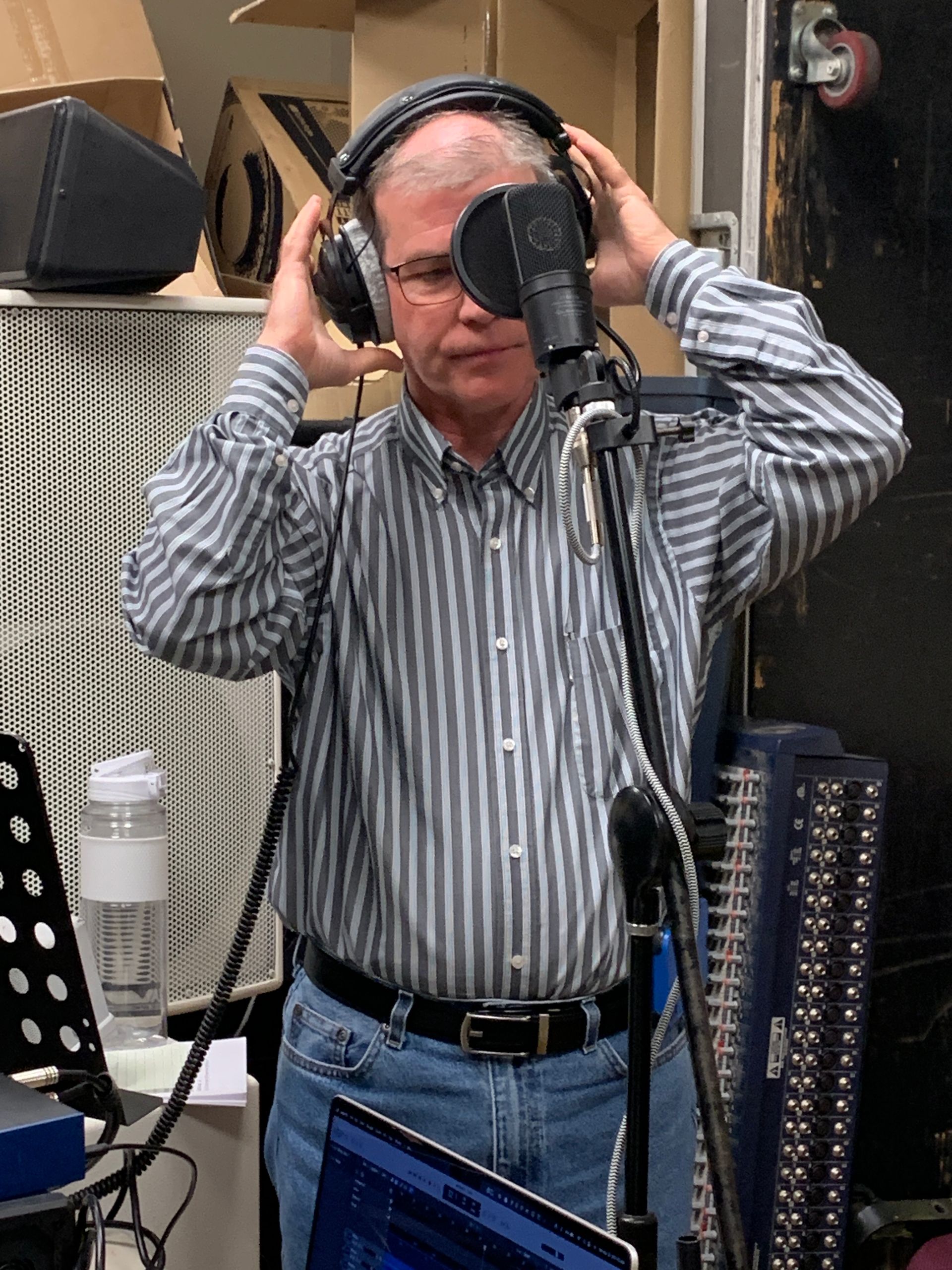 A man wearing headphones stands in front of a microphone