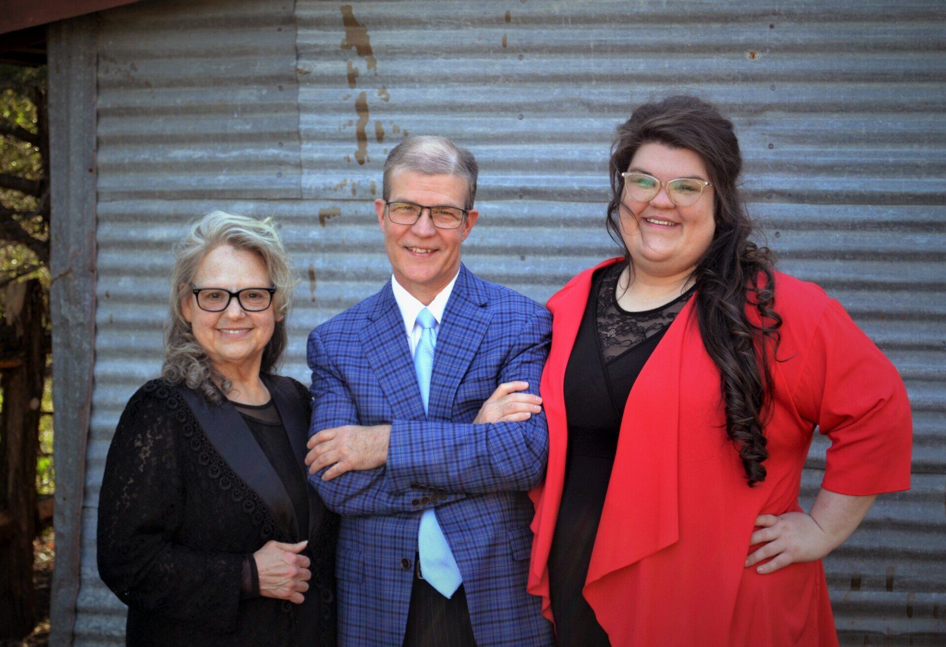 A man and two women are standing next to each other in front of a metal wall.