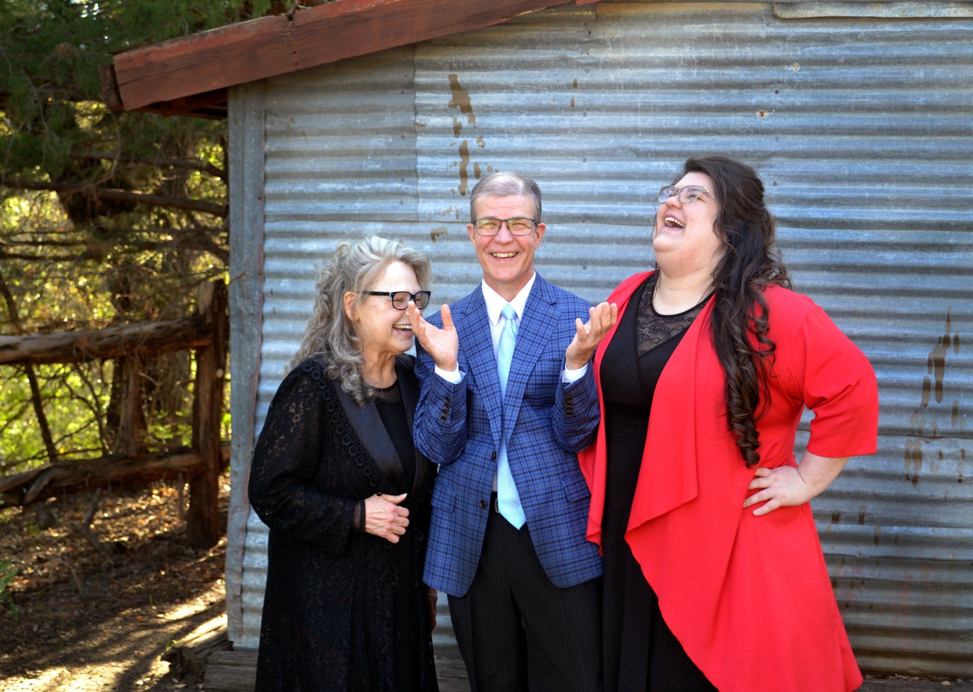 A man and two women are standing next to each other in front of a tin shed.