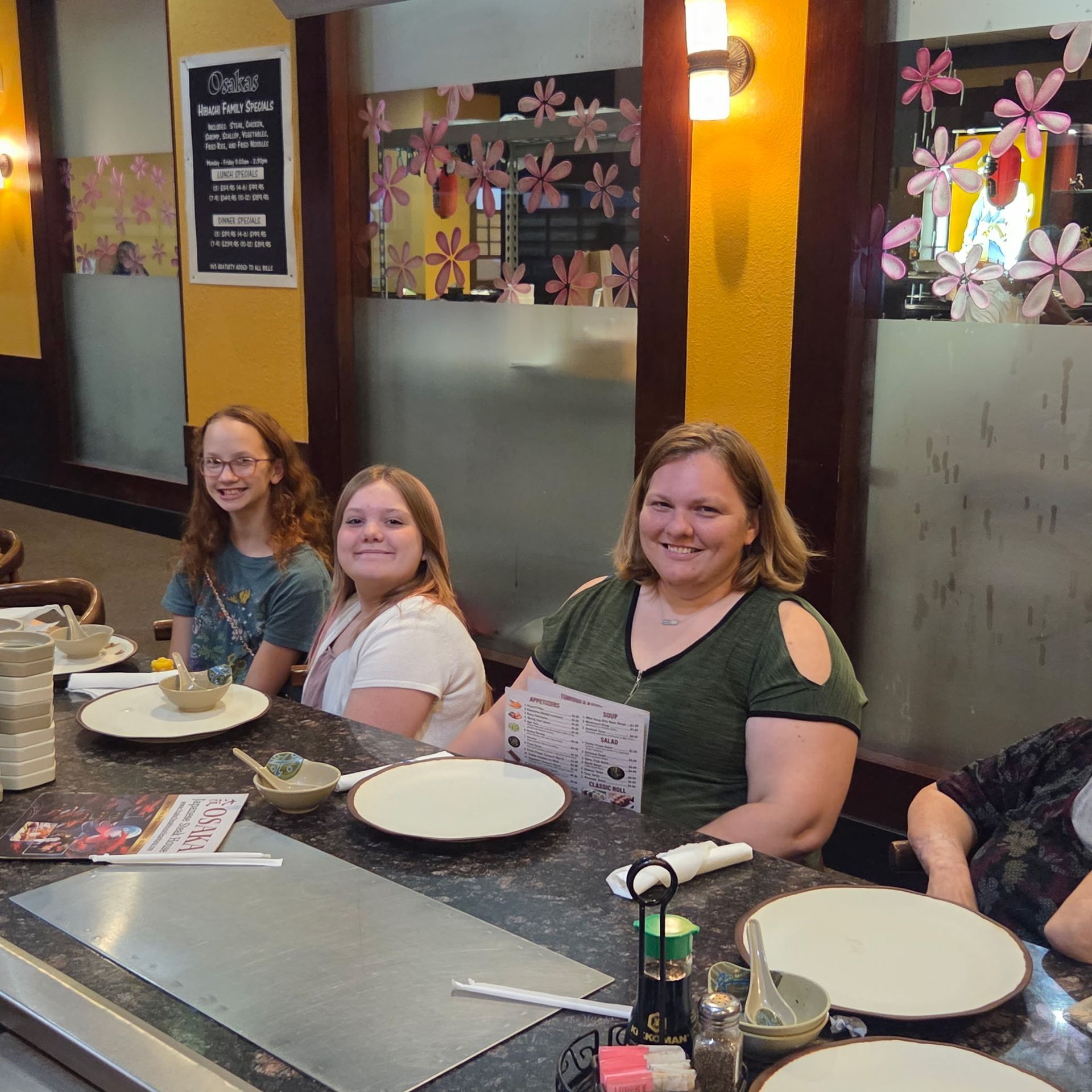 Three people seated at a teppanyaki grill table, smiling. Restaurant setting with dishes set up.