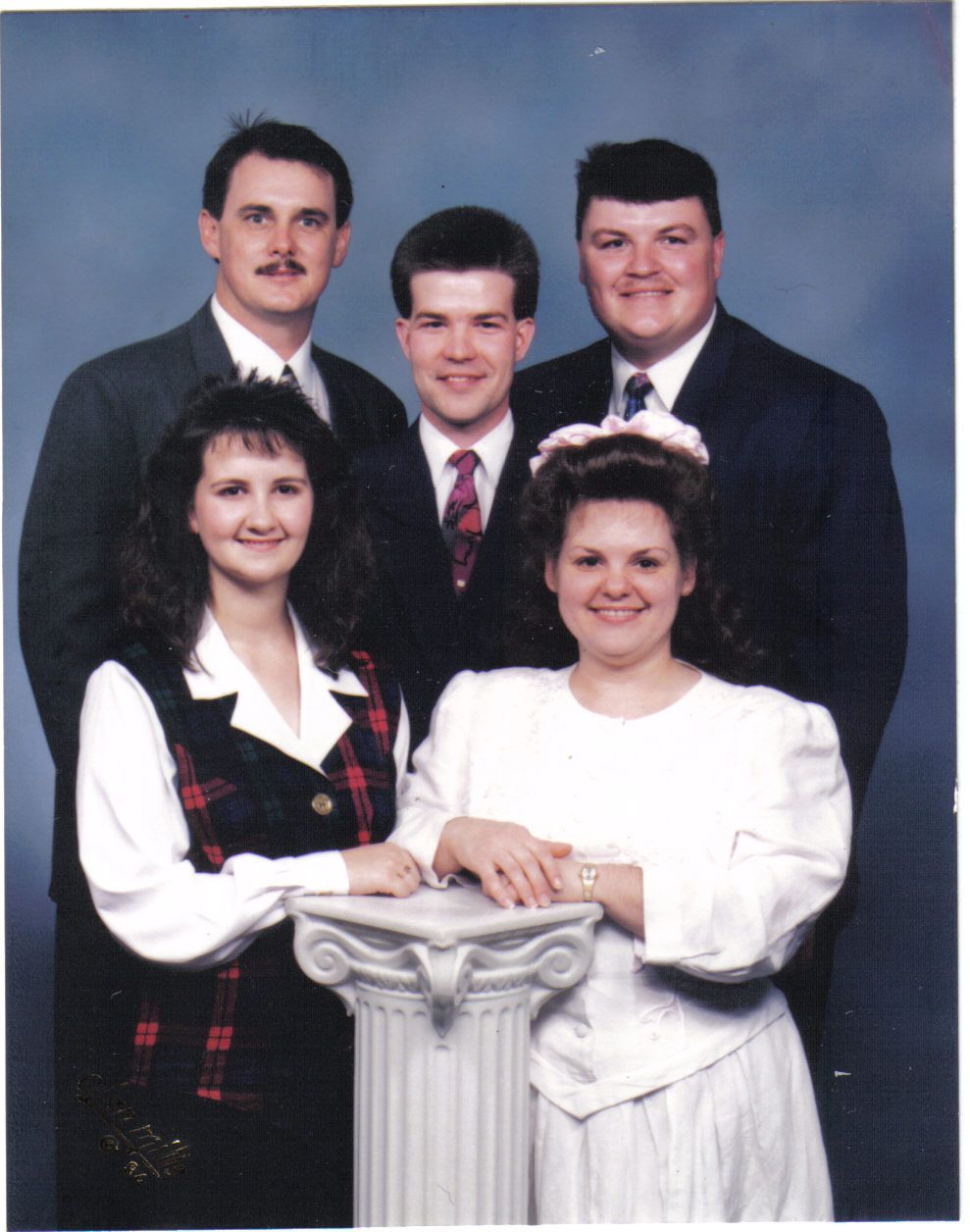Group of five people, posing formally. Two women in the front, three men behind them. All are smiling and dressed up.