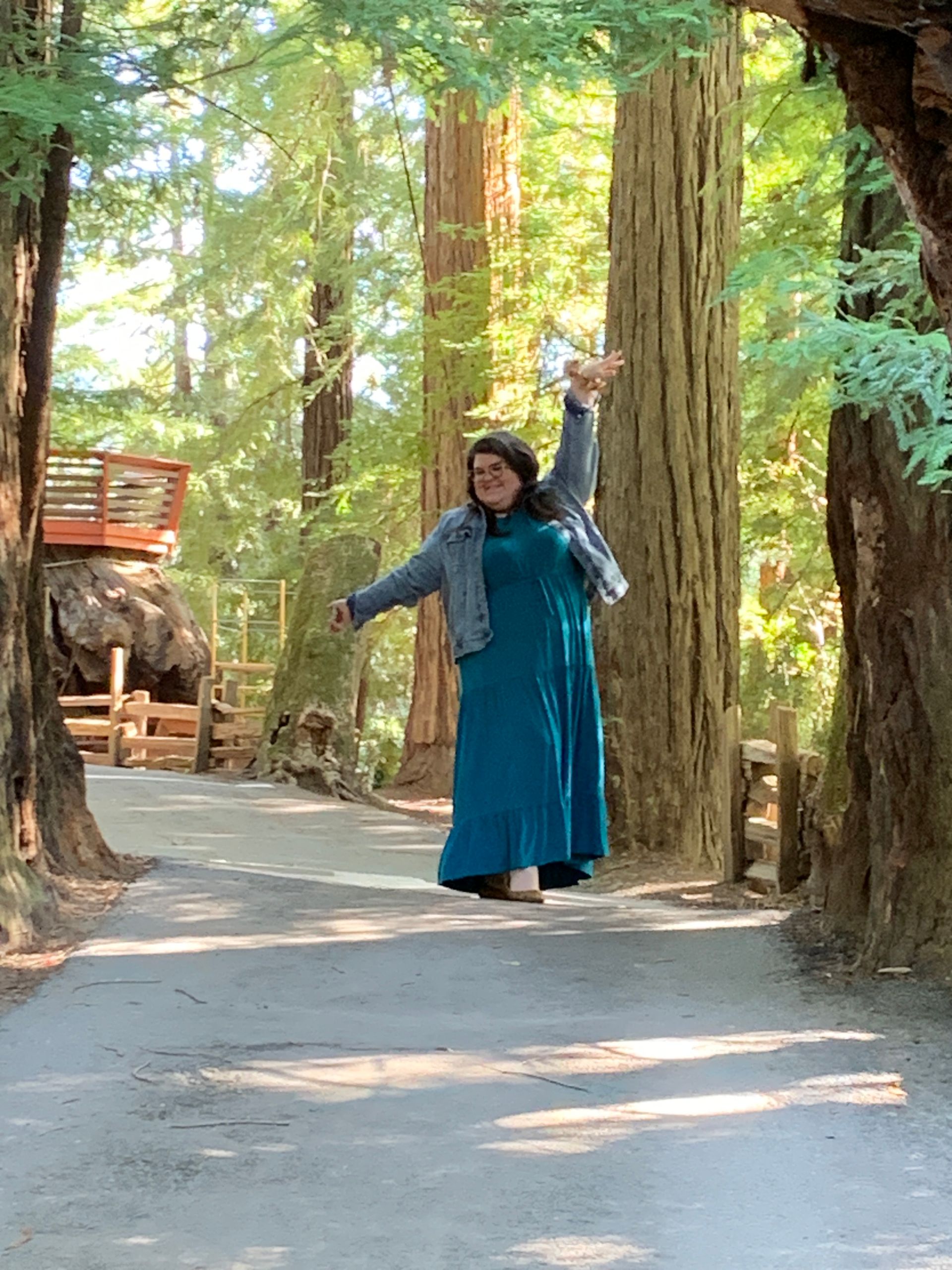 A woman in a blue dress is standing in the middle of a forest with her arms outstretched.