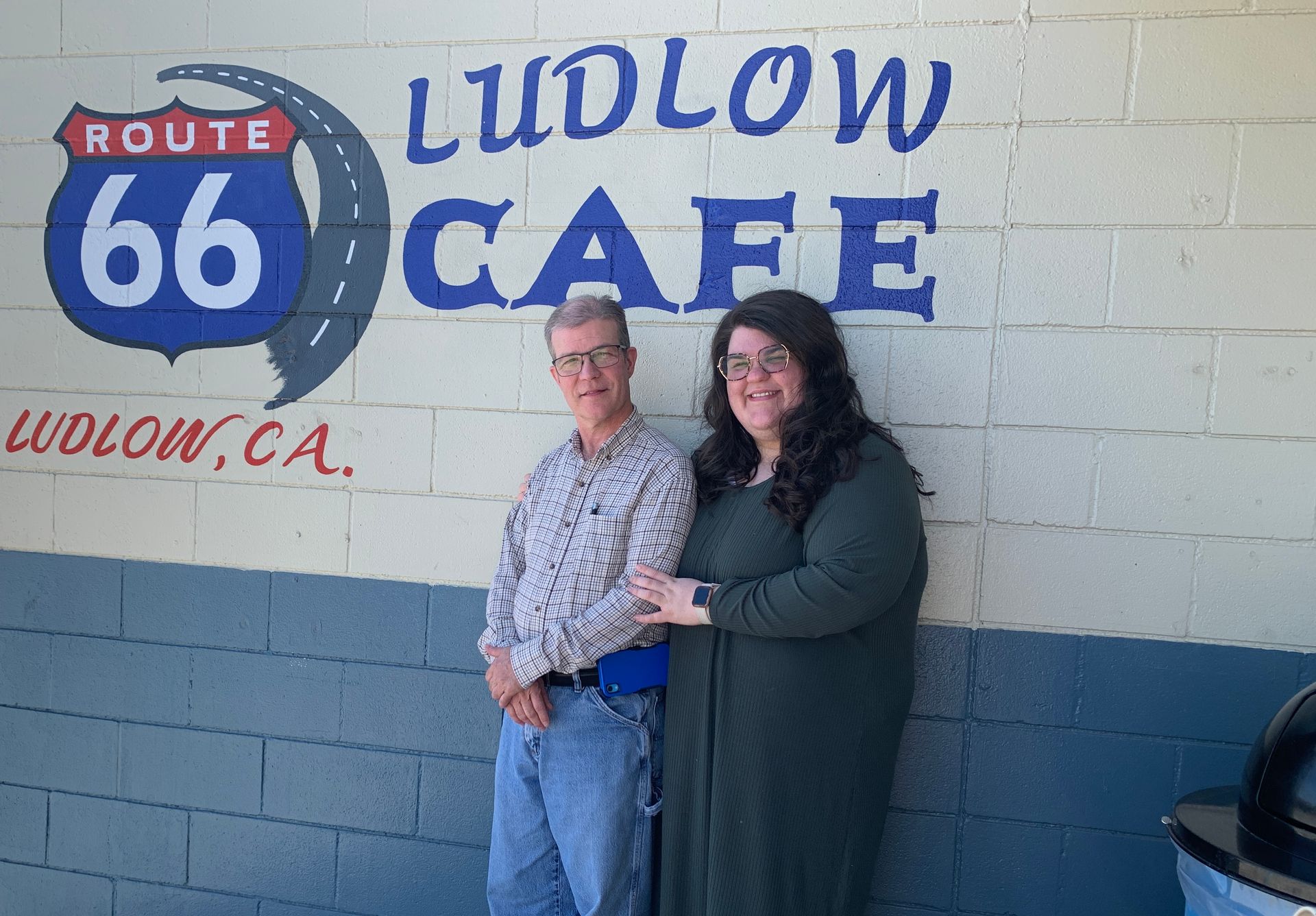 A man and a woman are standing in front of a sign for ludlow cafe