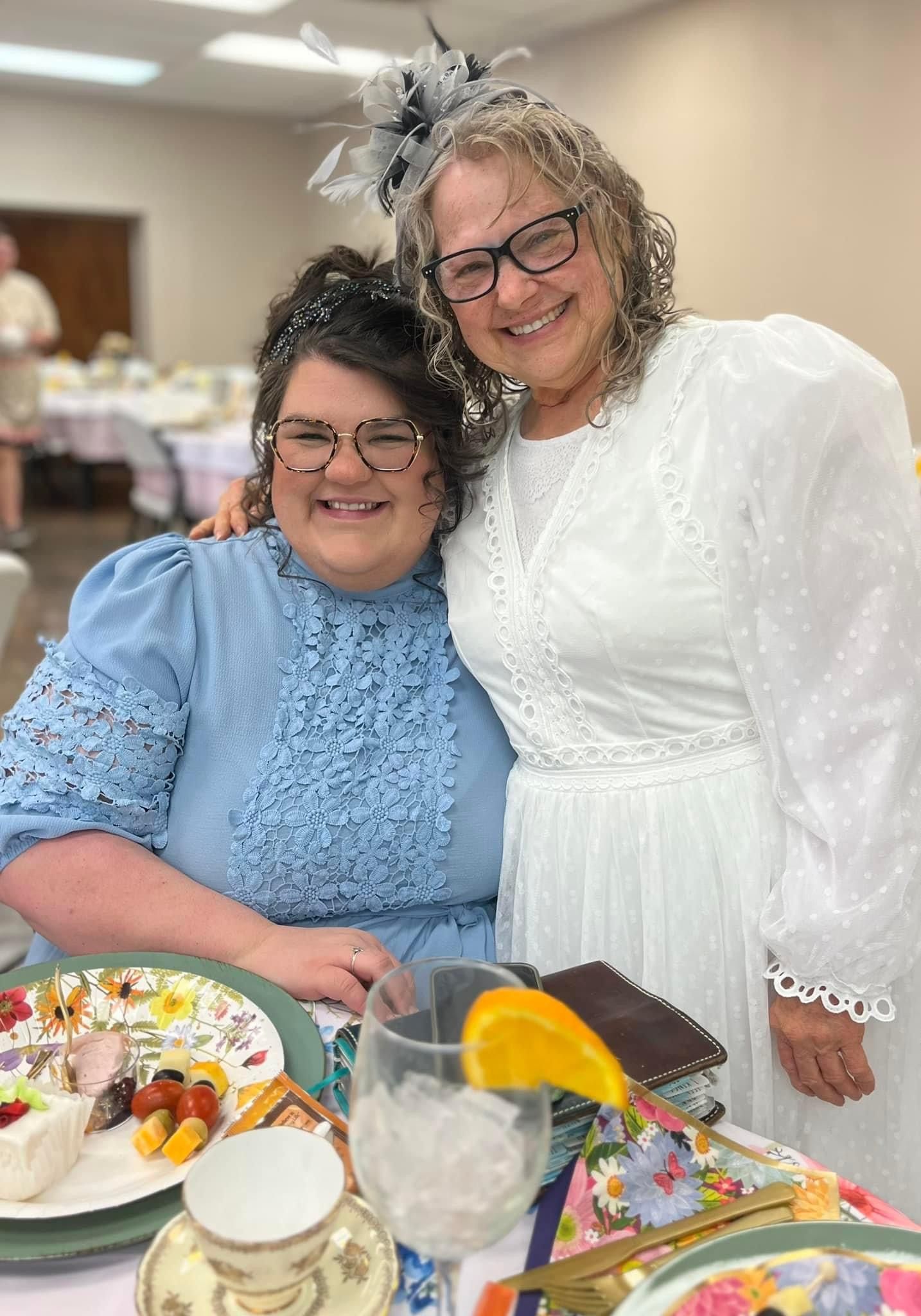 Two women are posing for a picture while sitting at a table.