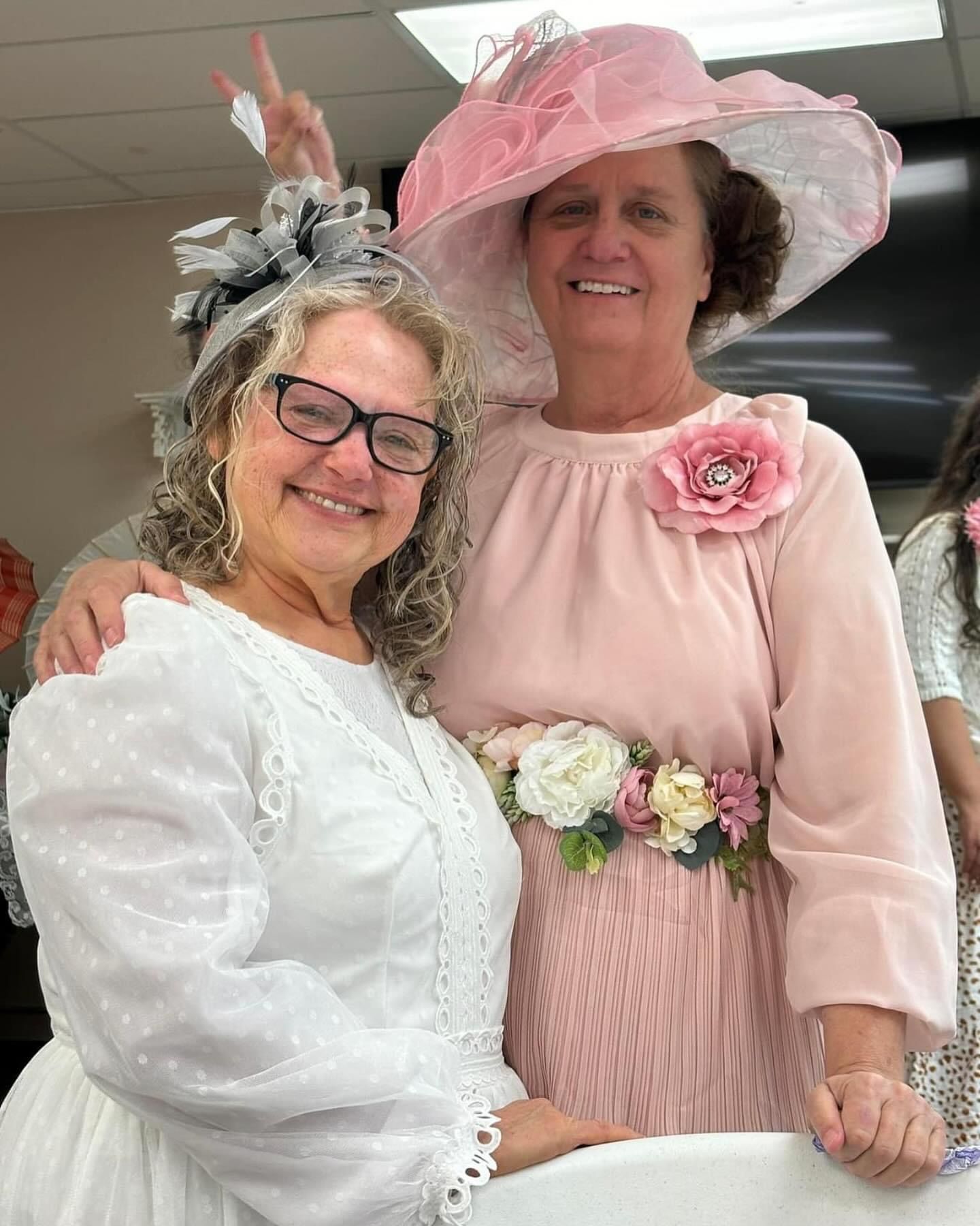 Two women wearing hats and dresses are posing for a picture.