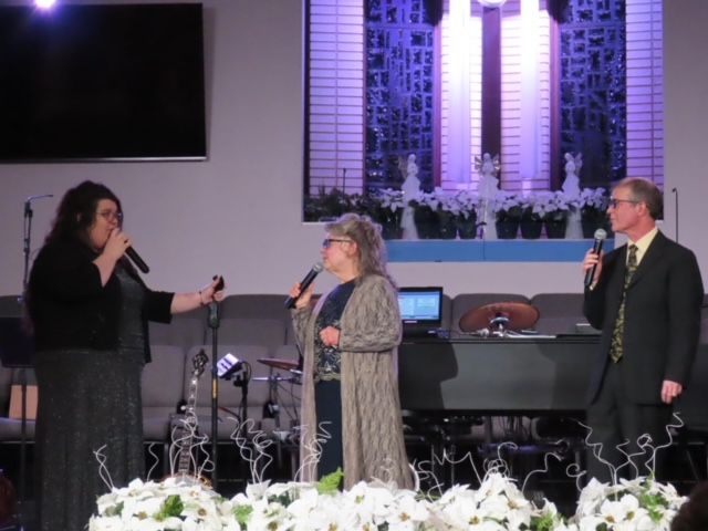 A man and two women singing into microphones on a stage