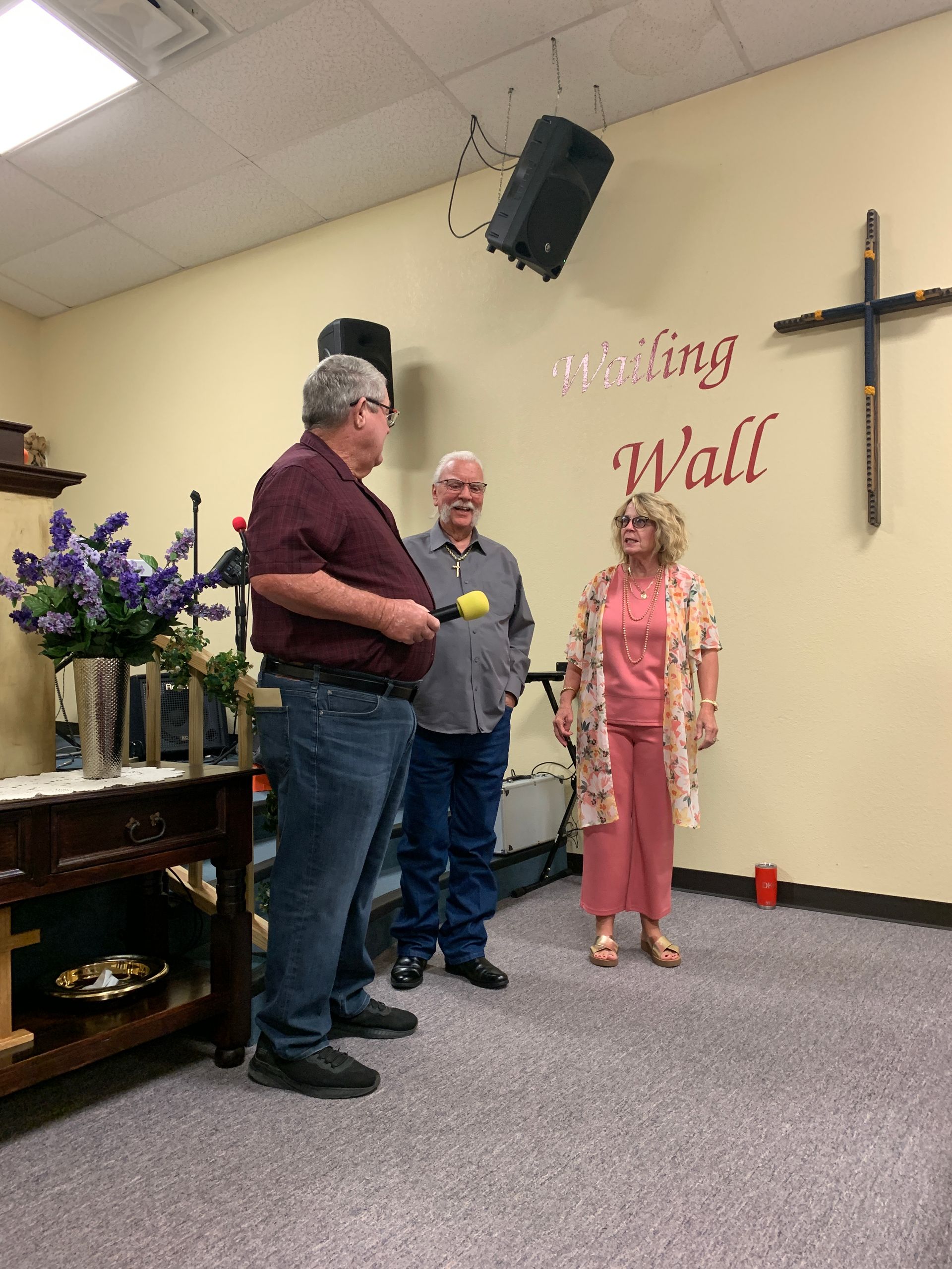 3 people standing beside a wall with a cross on it