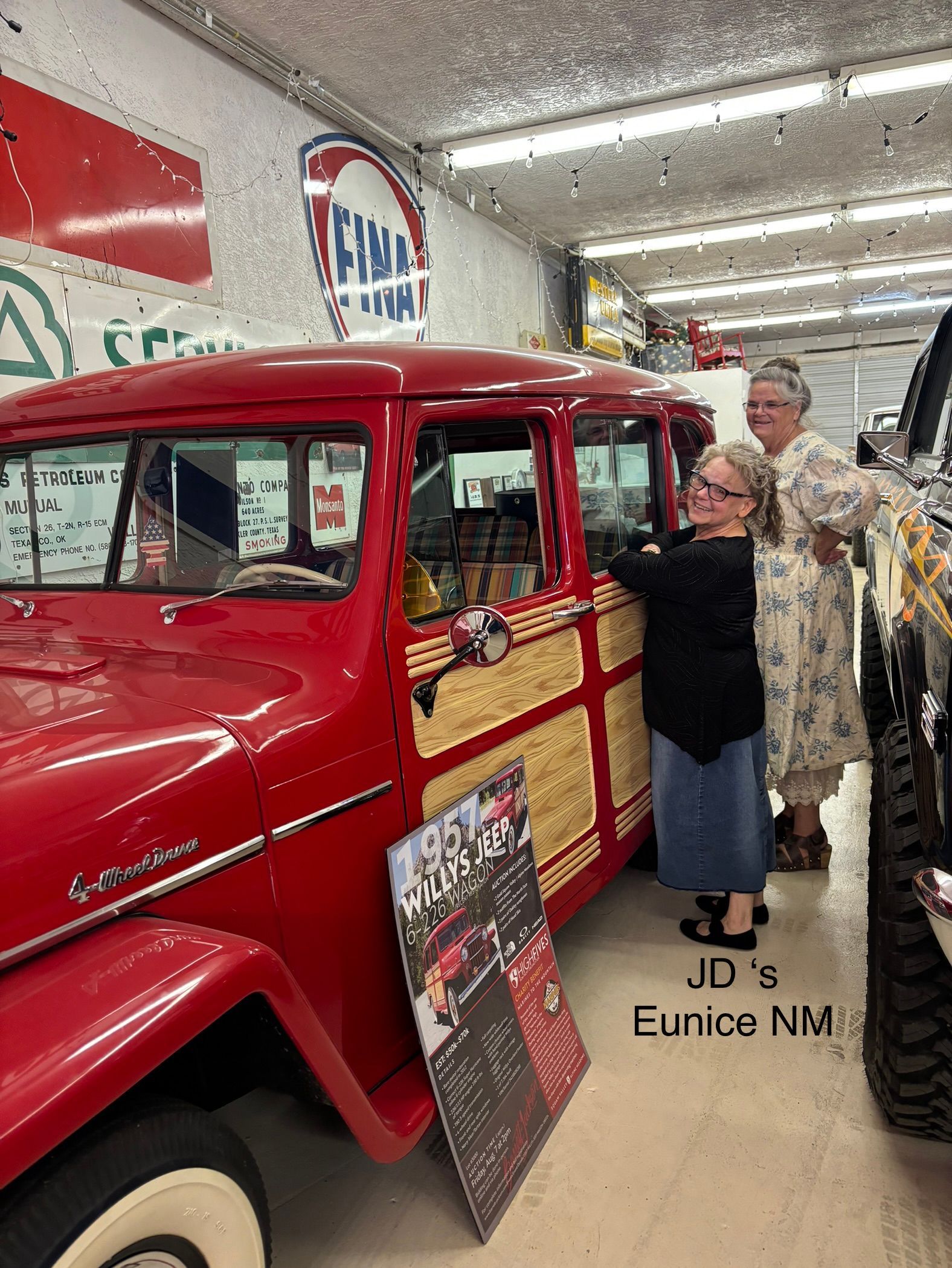 Two women are standing next to a red truck in a garage.