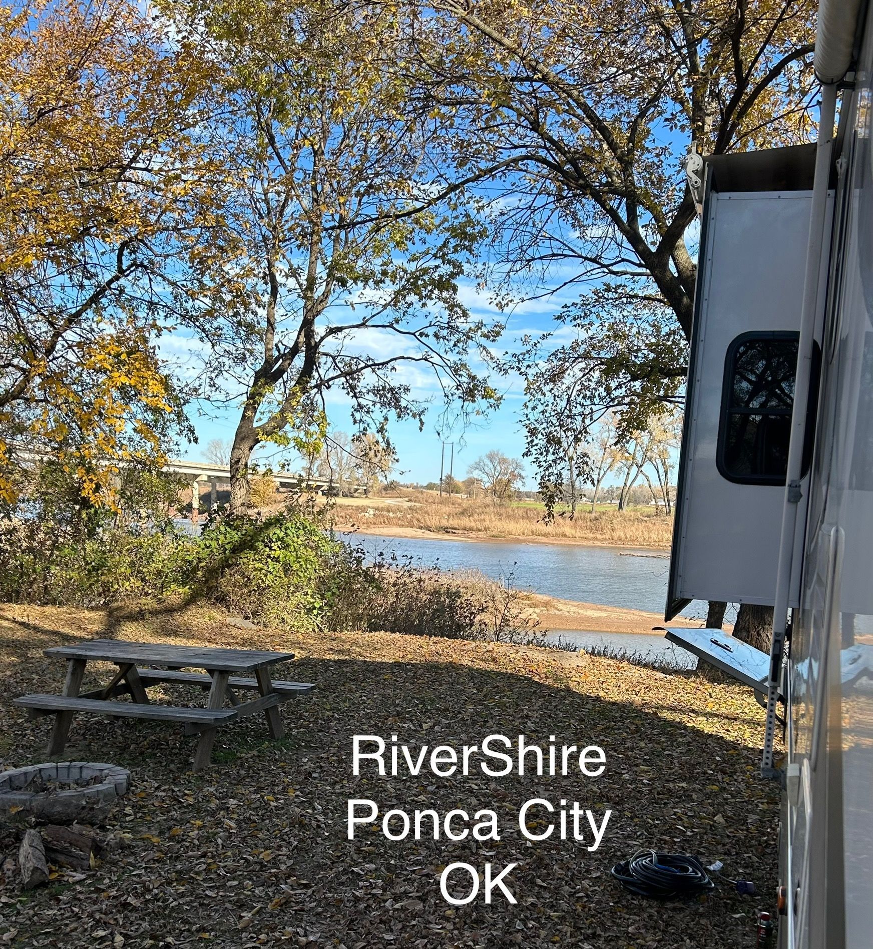 RV slide out showing on bank of river with pick nick table and firepit