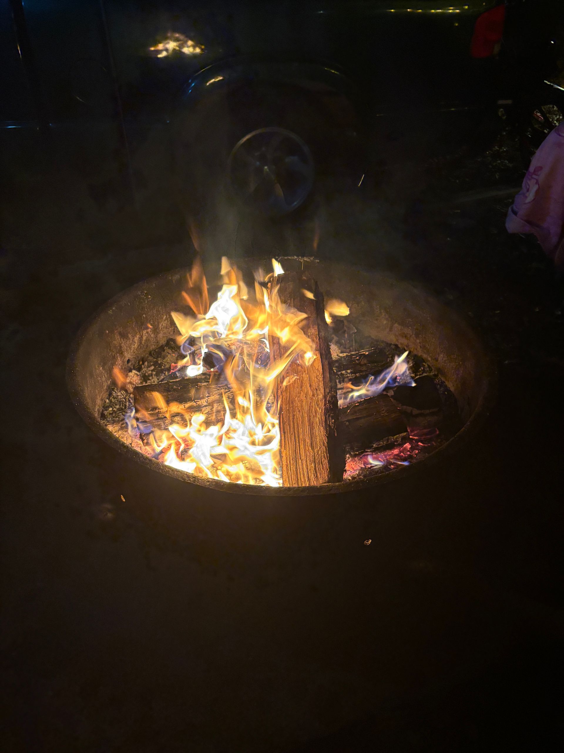 Fire burning in a circular metal fire pit at night, with flames and smoke rising.