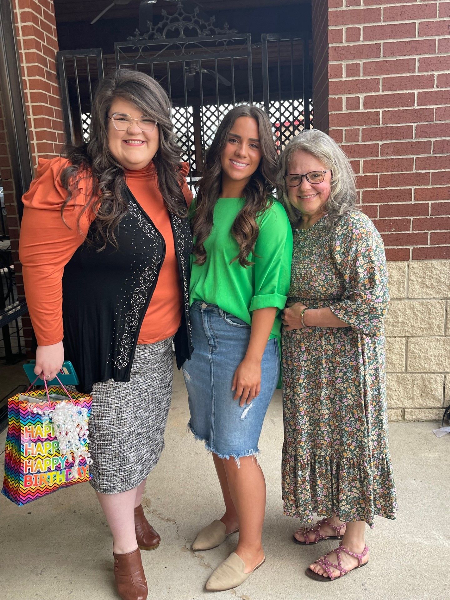 Three women are posing for a picture in front of a brick building.