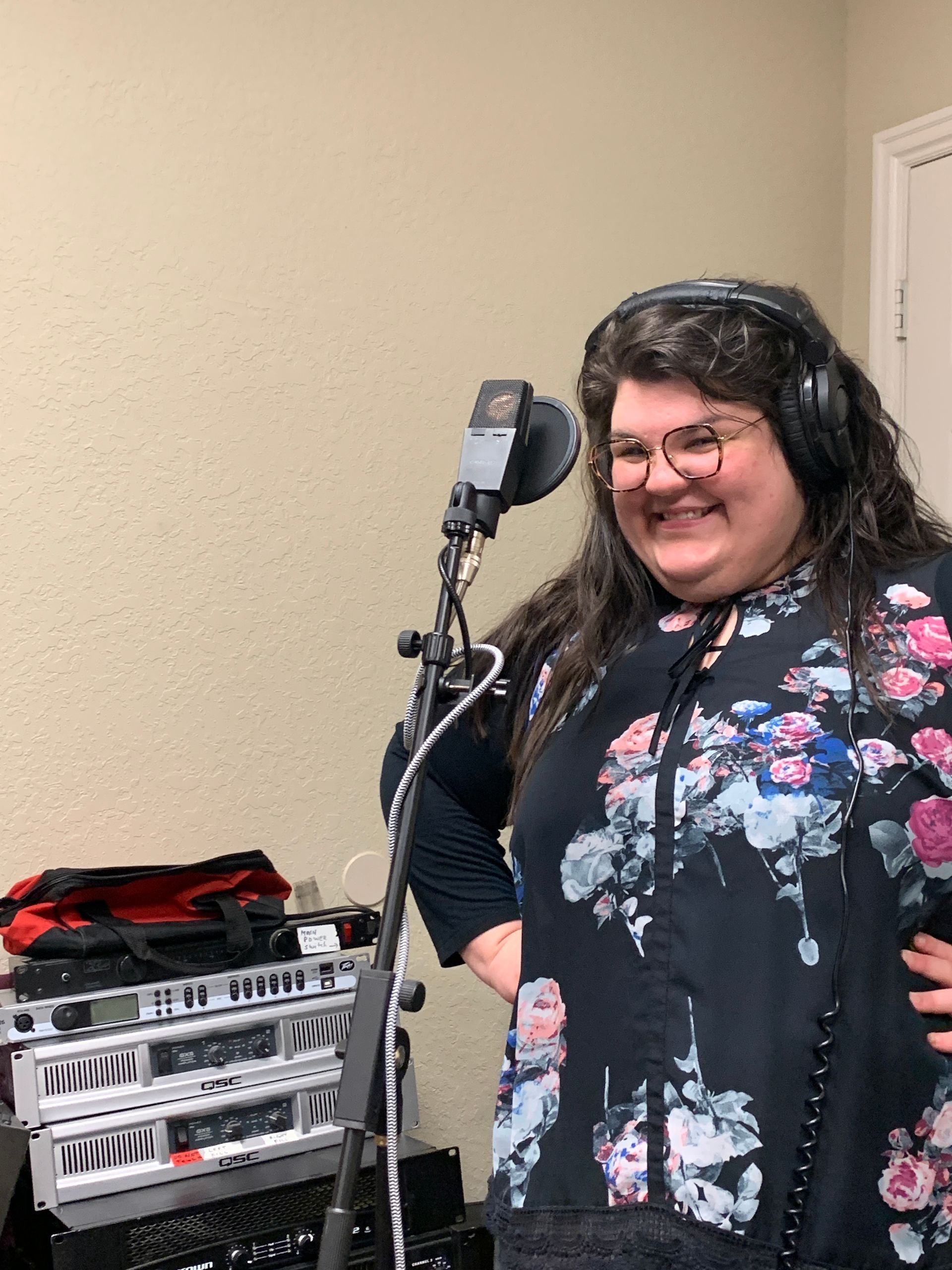 A woman wearing headphones is standing in front of a microphone.
