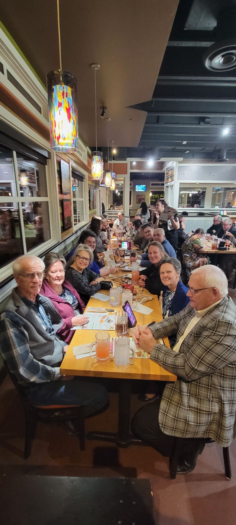 People seated at a long table in a restaurant. Overhead pendant lights.