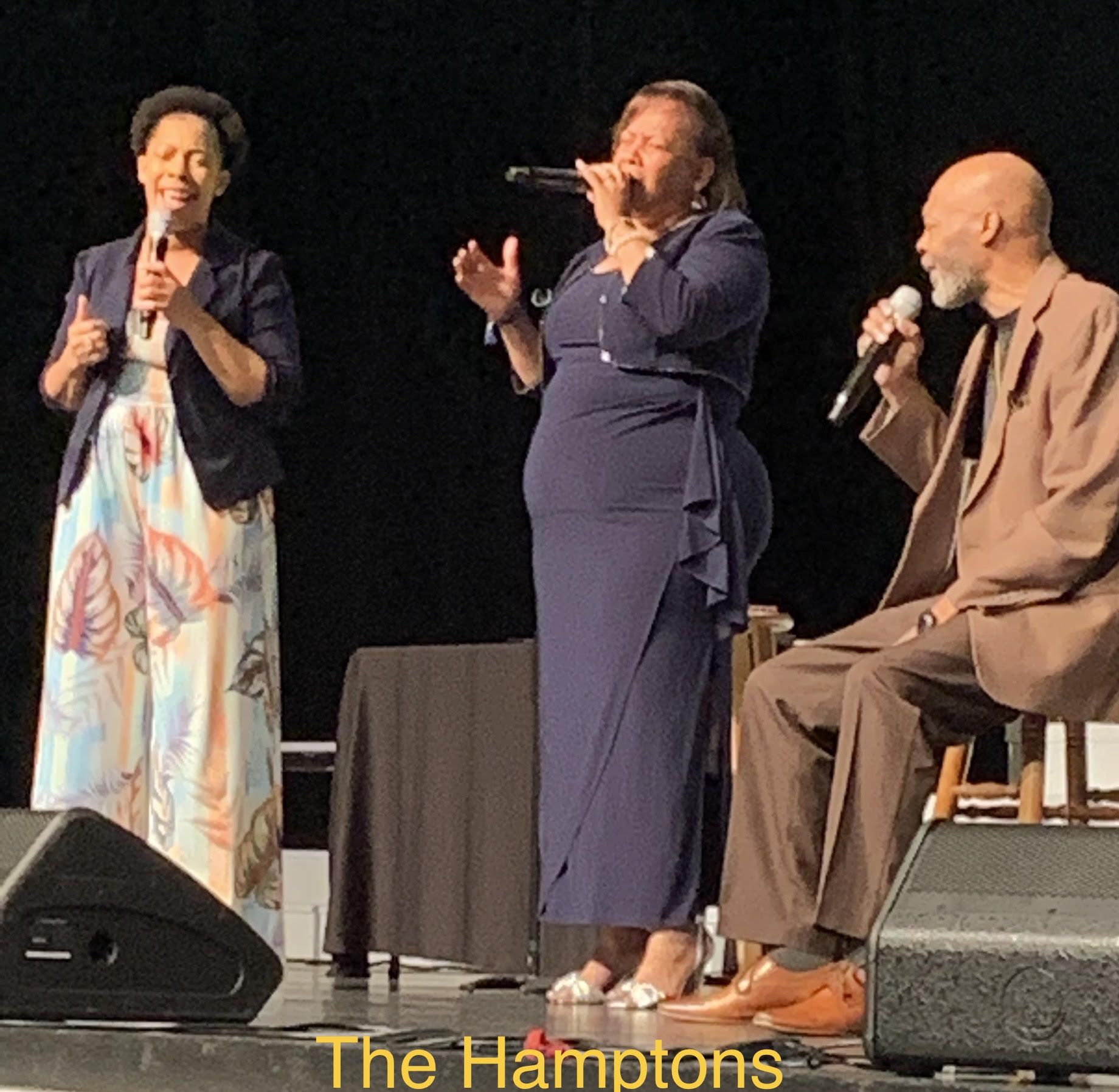 A group of people singing on a stage with the hamptons written on the bottom