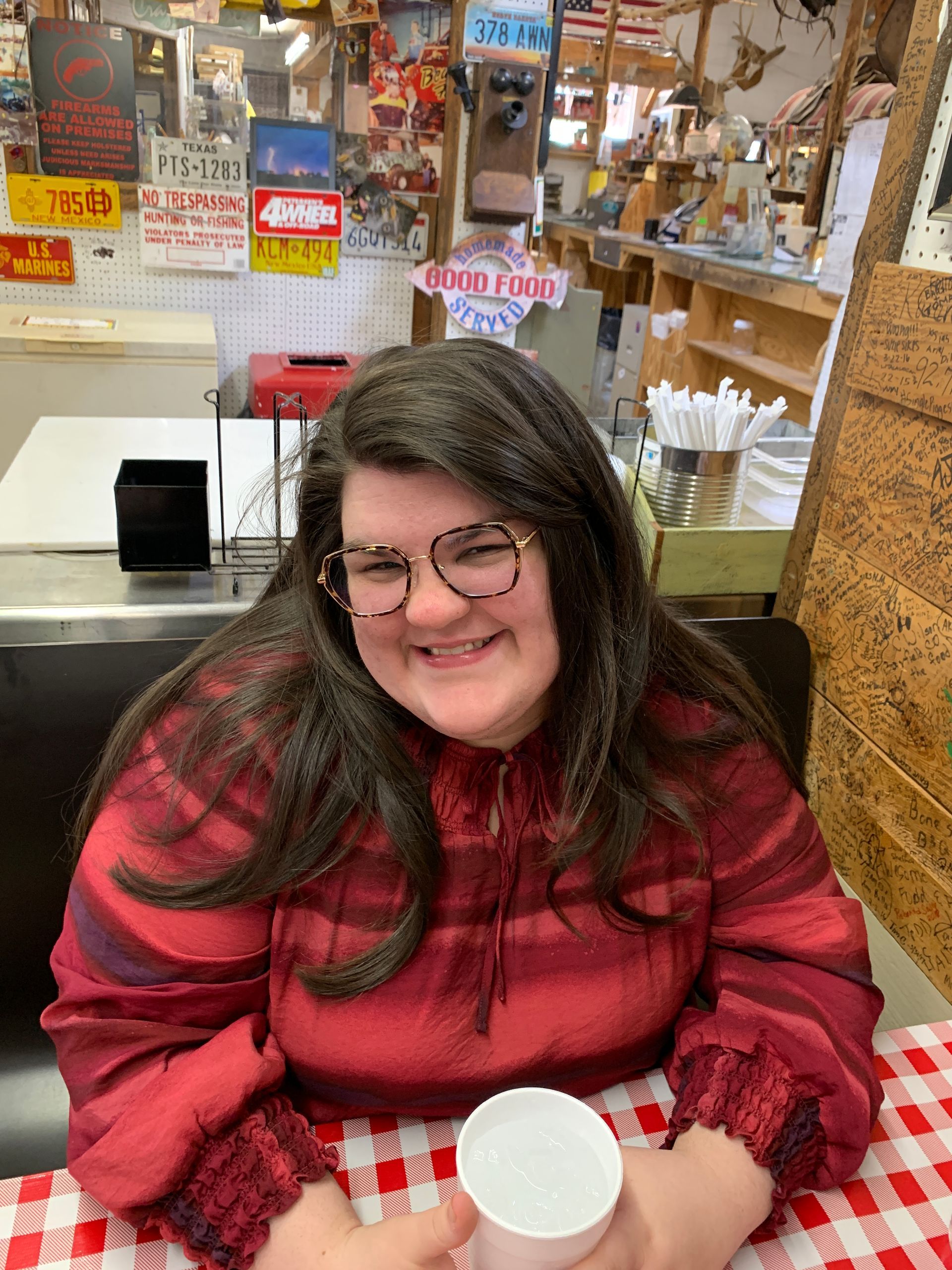 A woman wearing glasses is sitting at a table holding a cup of coffee.