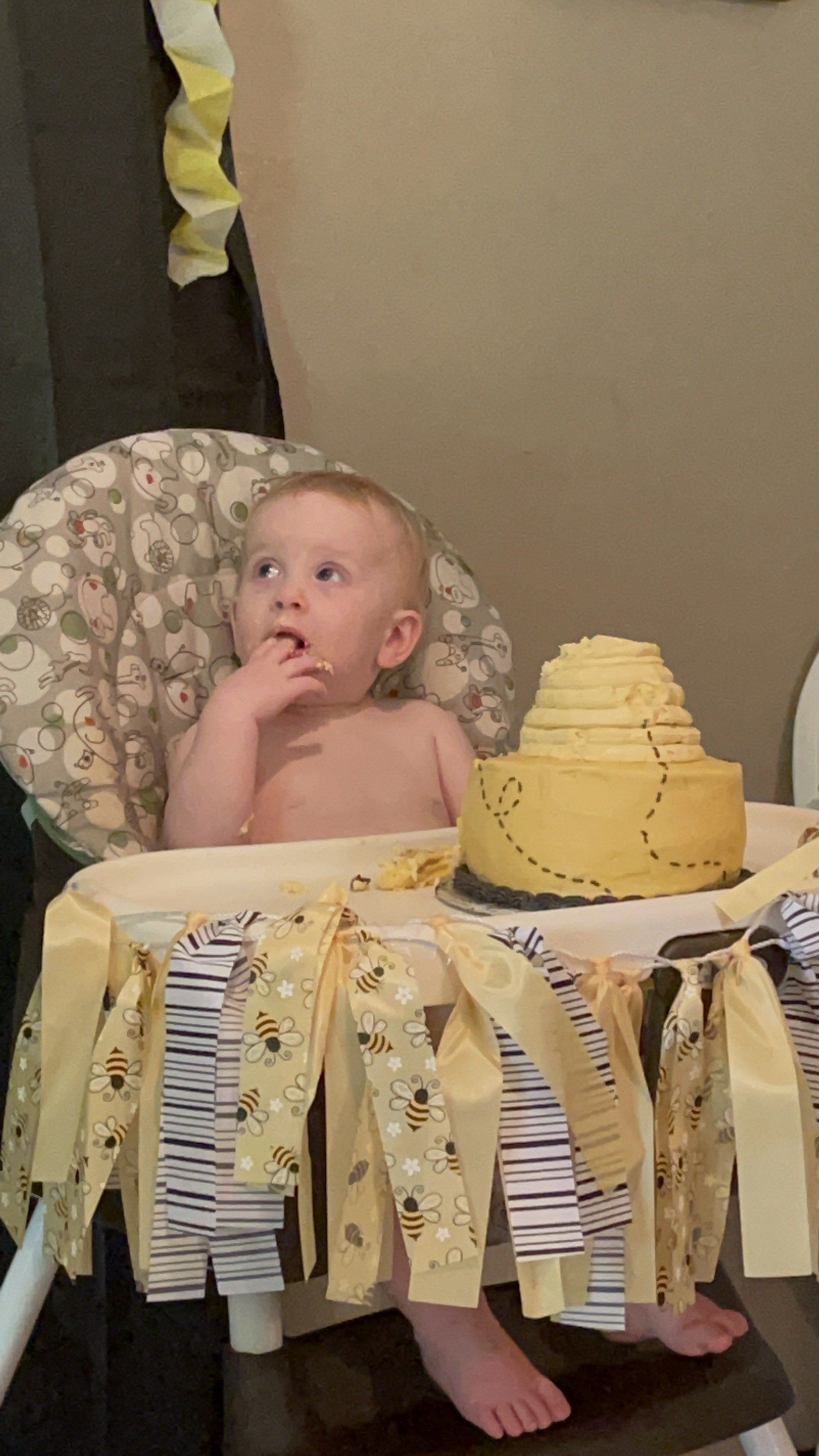 A baby is sitting in a high chair next to a cake.