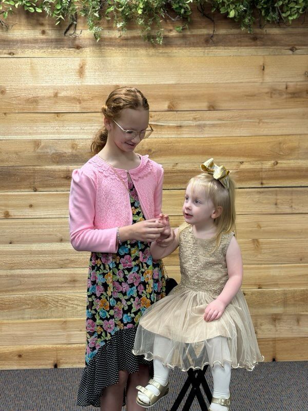 Two little girls are standing next to each other in front of a wooden wall.