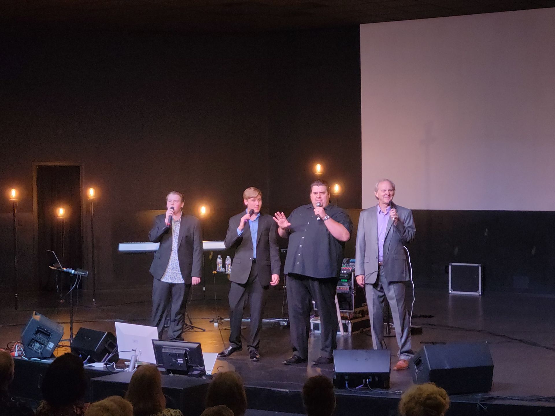 A group of men are standing on a stage singing into microphones.