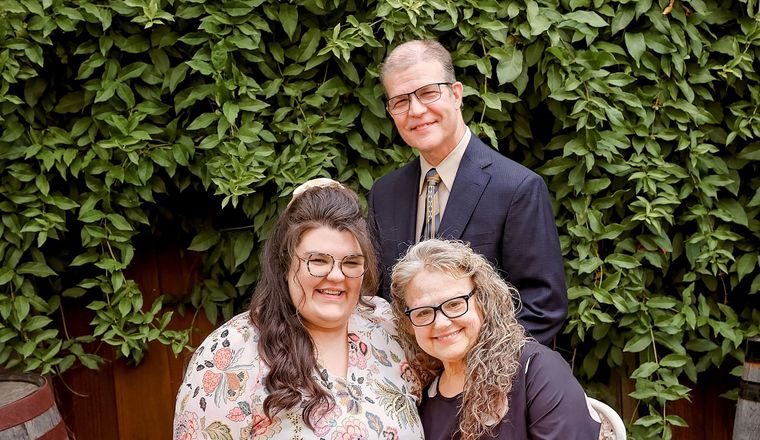 A man and two women are posing for a picture in front of a bush.