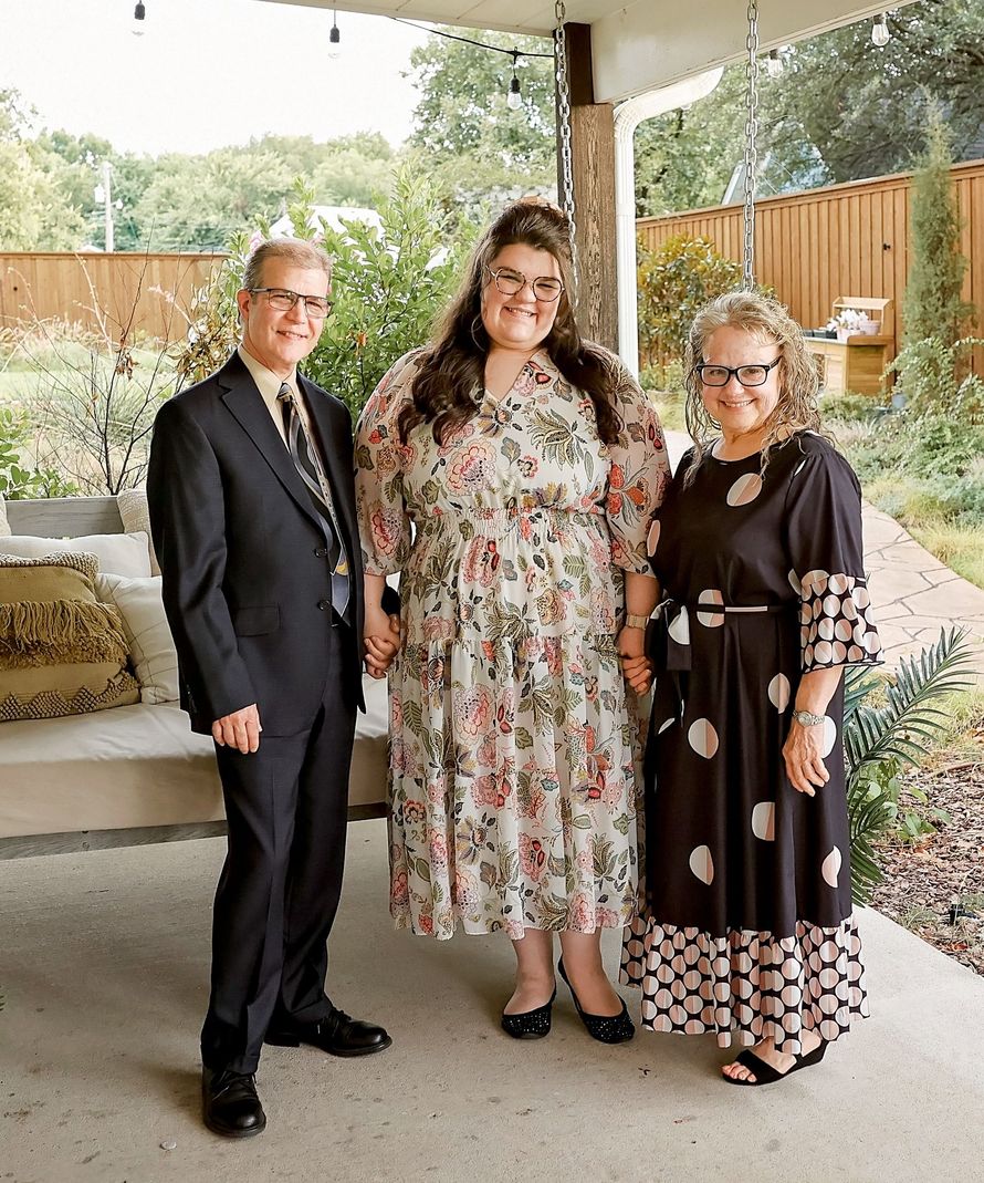 A man and two women are standing on a porch holding hands