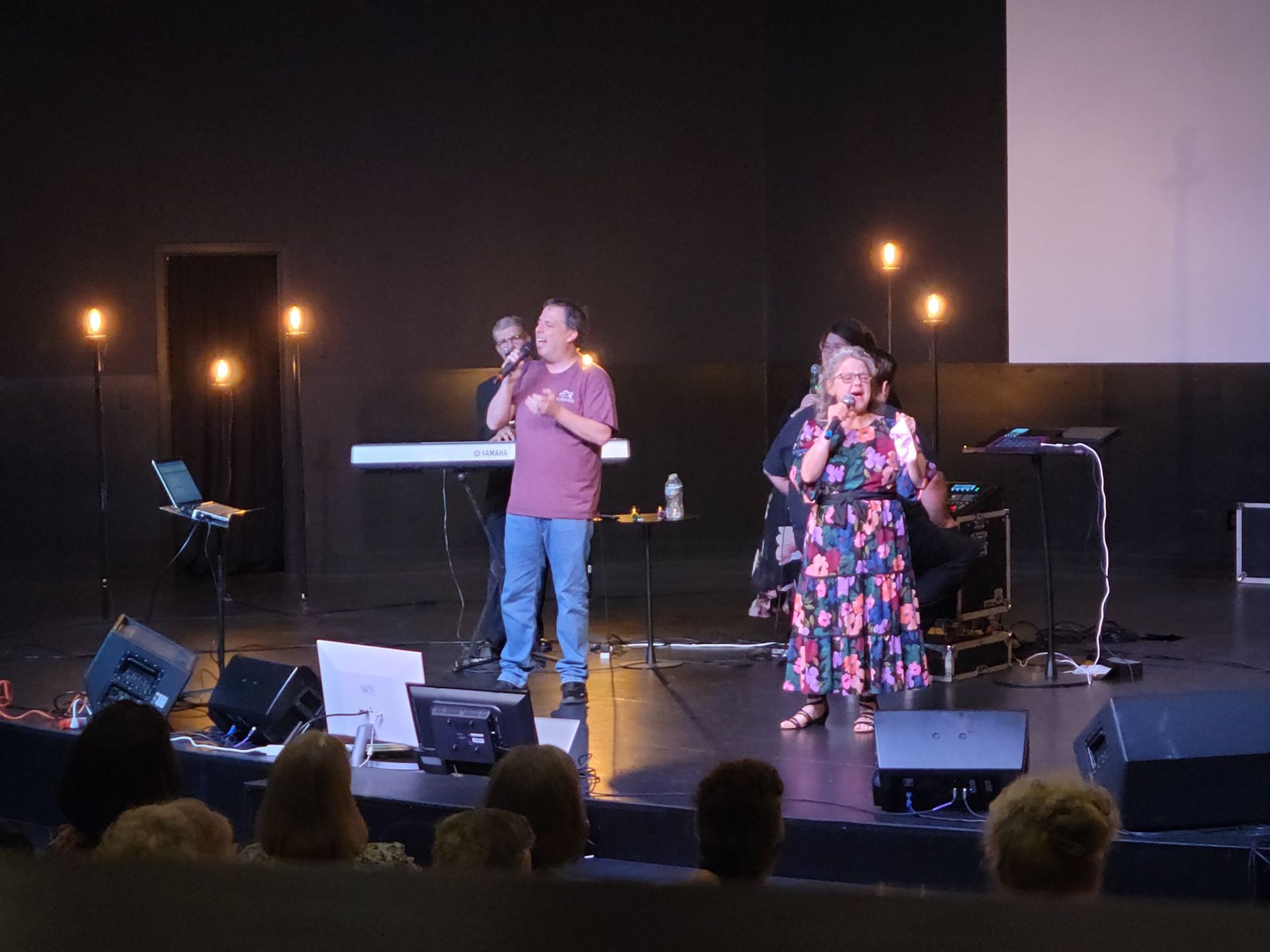 A group of people are standing on a stage singing into microphones.