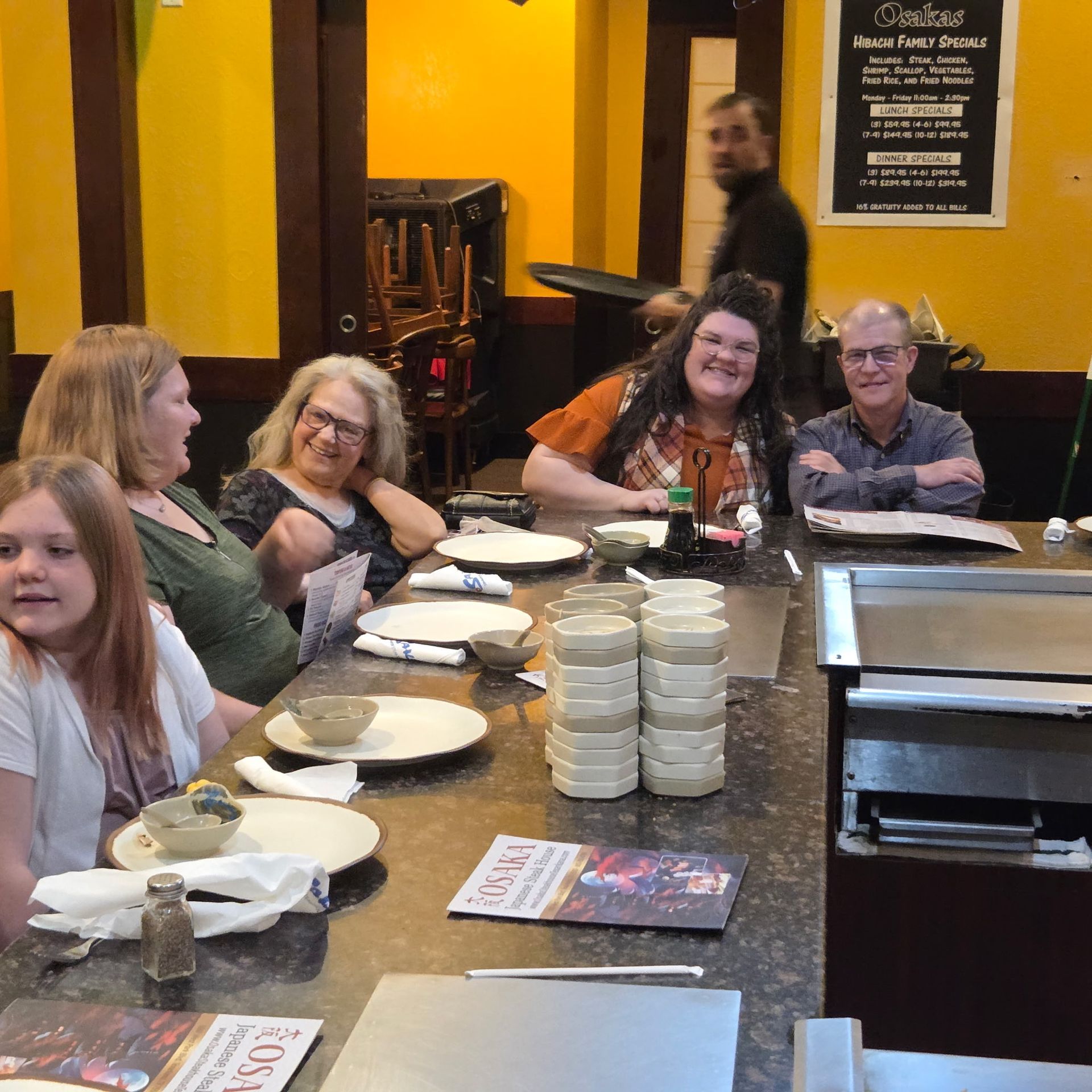 Group seated around a hibachi grill in a restaurant, anticipating a meal.