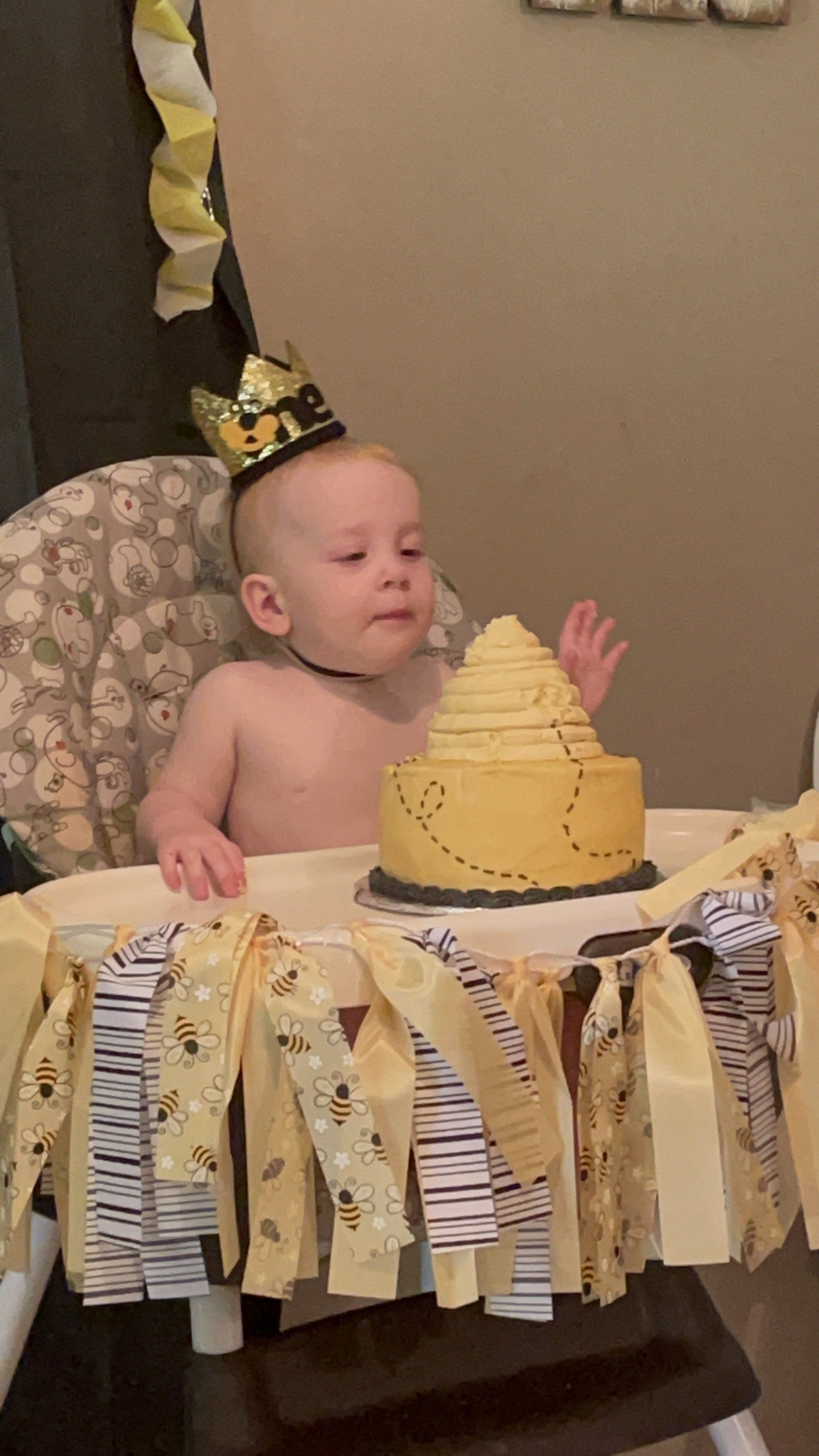 A baby is sitting in a high chair next to a cake.