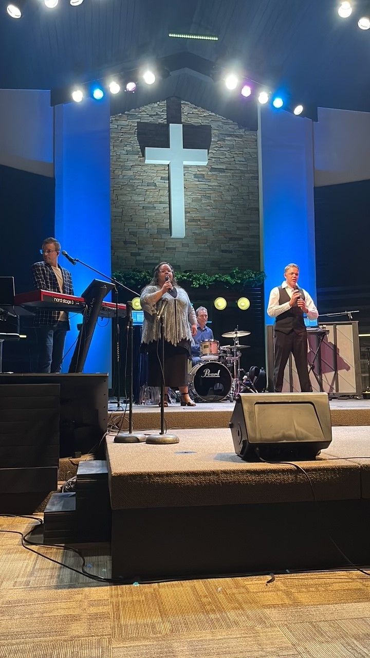 A group of people are standing on a stage in front of a cross.