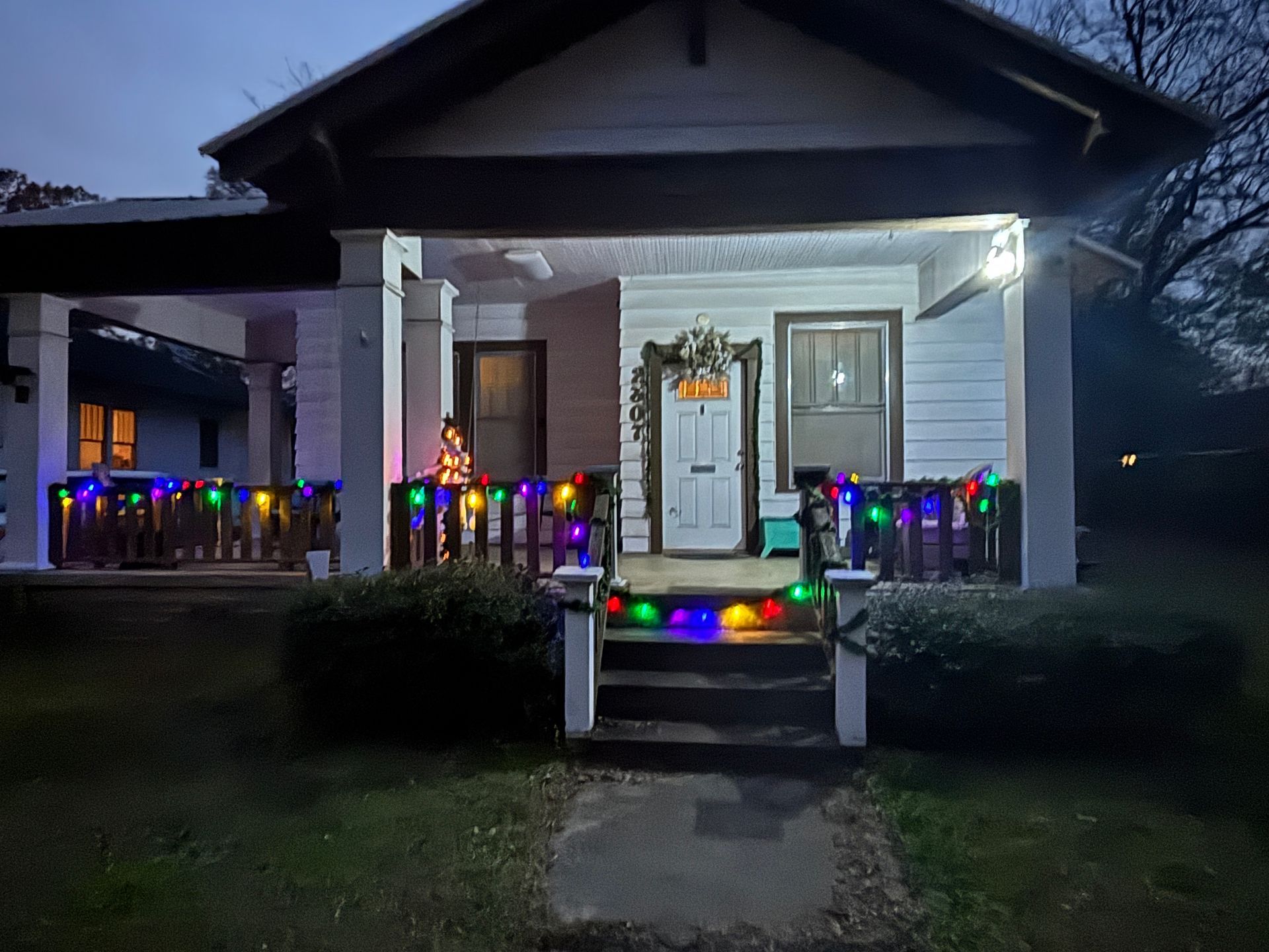 A house at dusk with colorful lights on the porch railing and doorway.