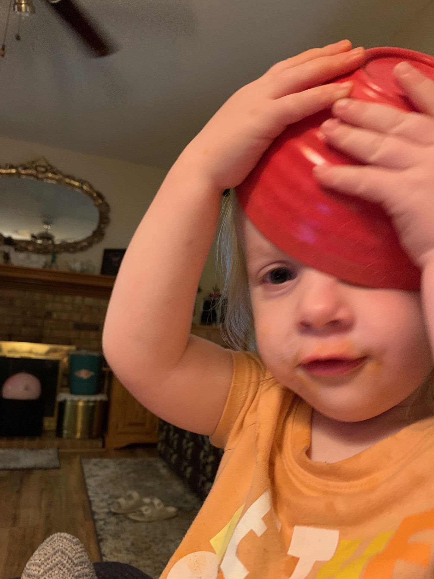 A little girl is holding a red bowl on her head