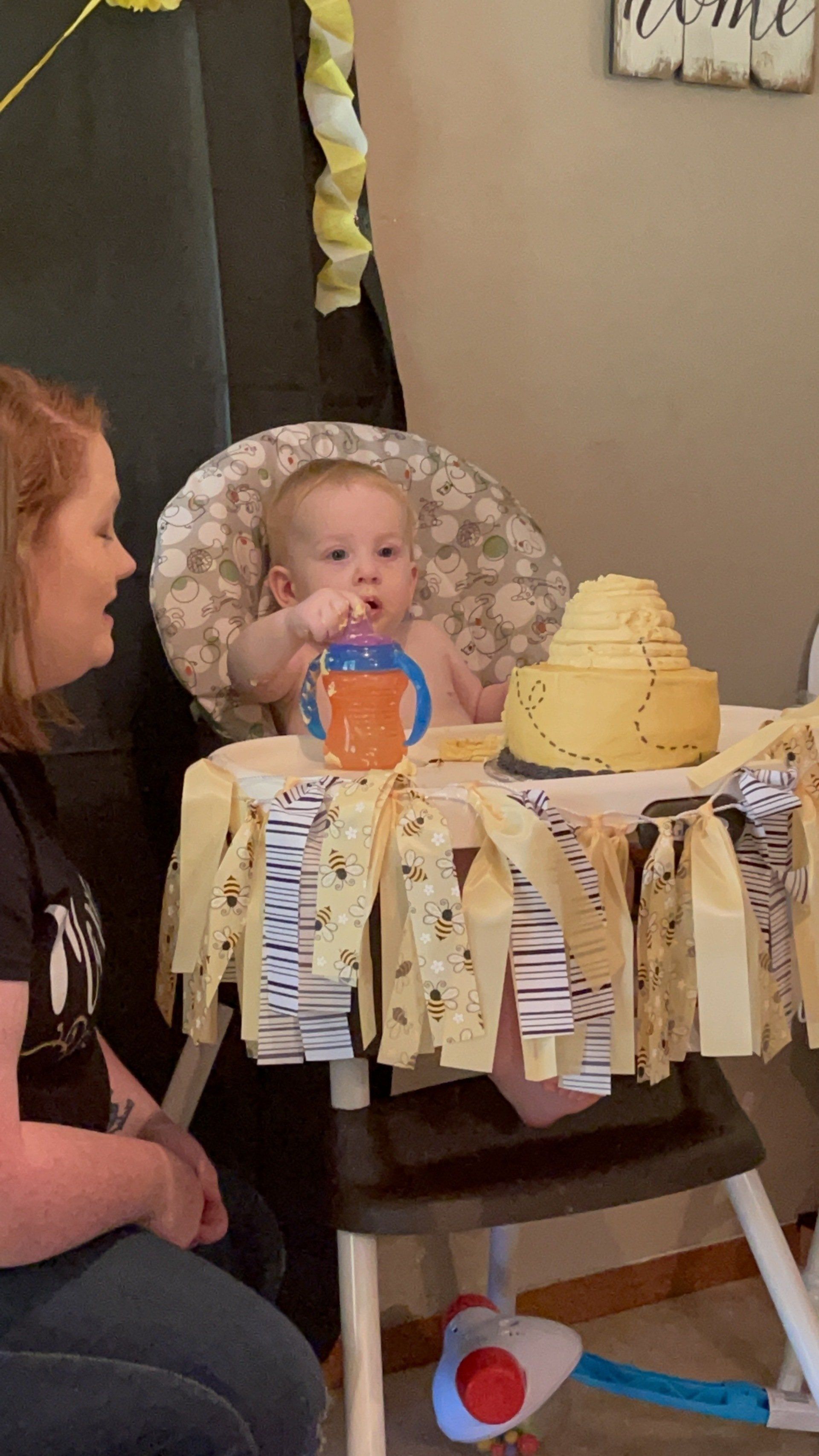 A woman is sitting next to a baby in a high chair eating a cake.