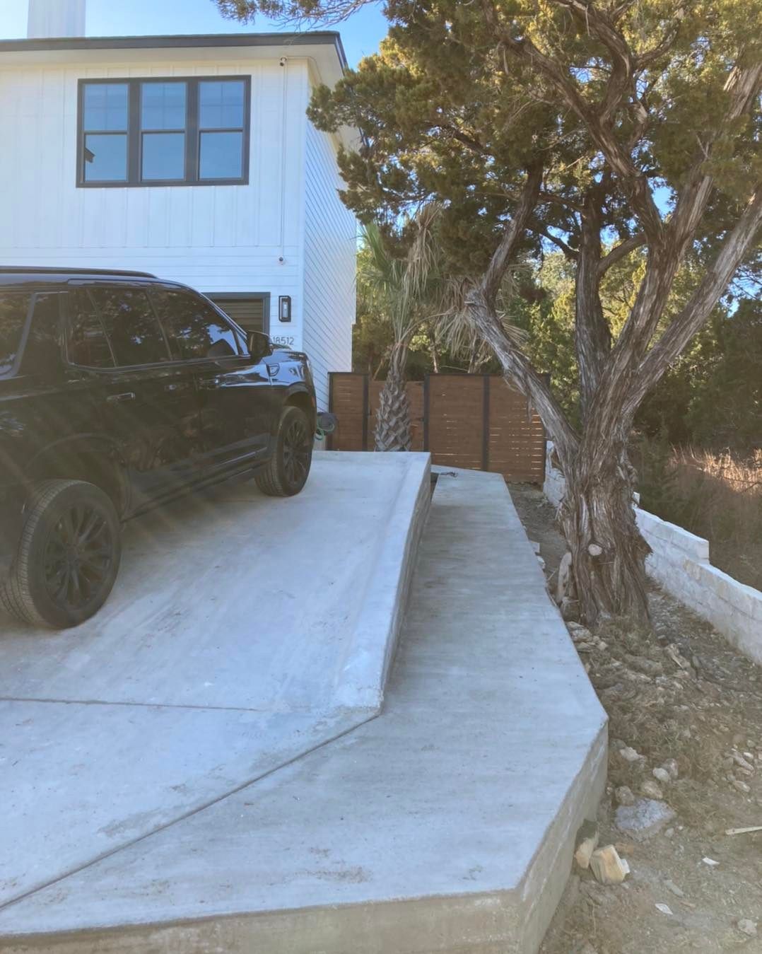 Black SUV parked on a concrete driveway in front of a white house with a tree alongside a walkway.