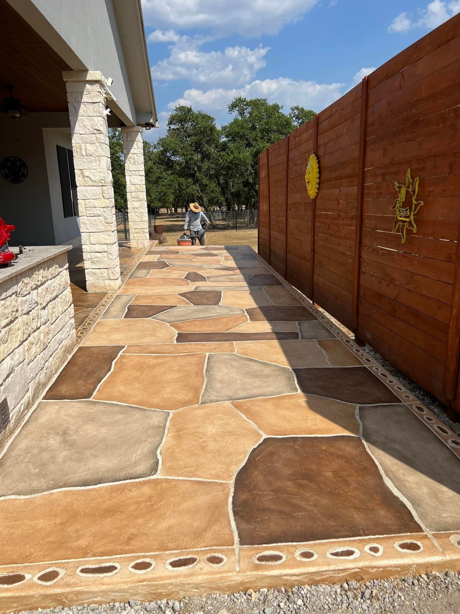 Stone pathway next to a wooden fence and house with a person in the distance.