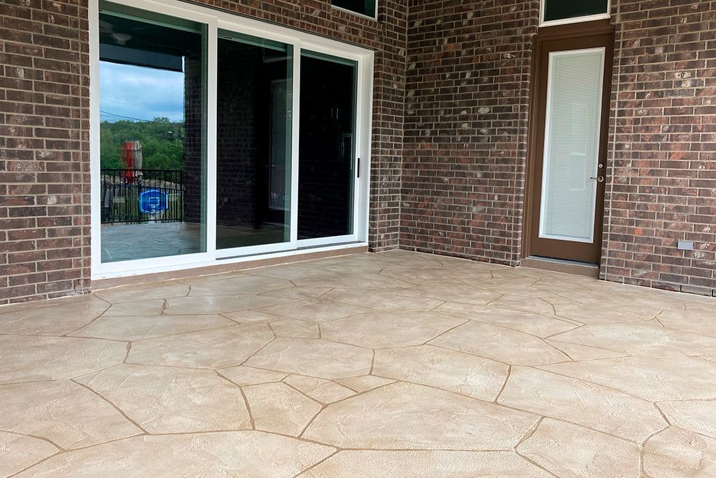 Patio with brown, textured concrete flooring, sliding glass door, and brick wall.