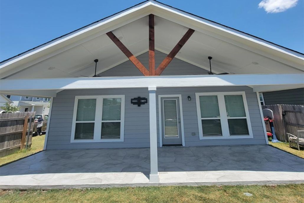 Blue house with carport, two windows, and a door under the gabled roof, on concrete slab.