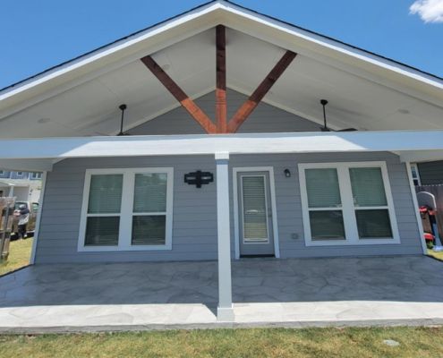 Gray house exterior with porch; brown wooden beams, white ceiling, and concrete patio.
