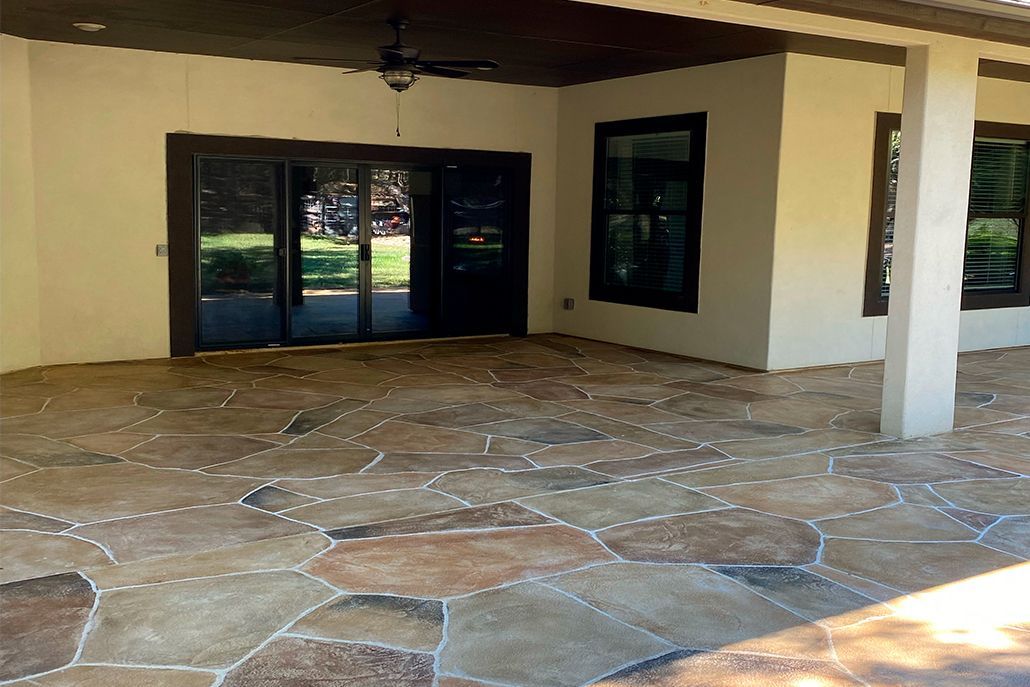 Covered patio with a stone-patterned floor, sliding glass doors, and a ceiling fan.
