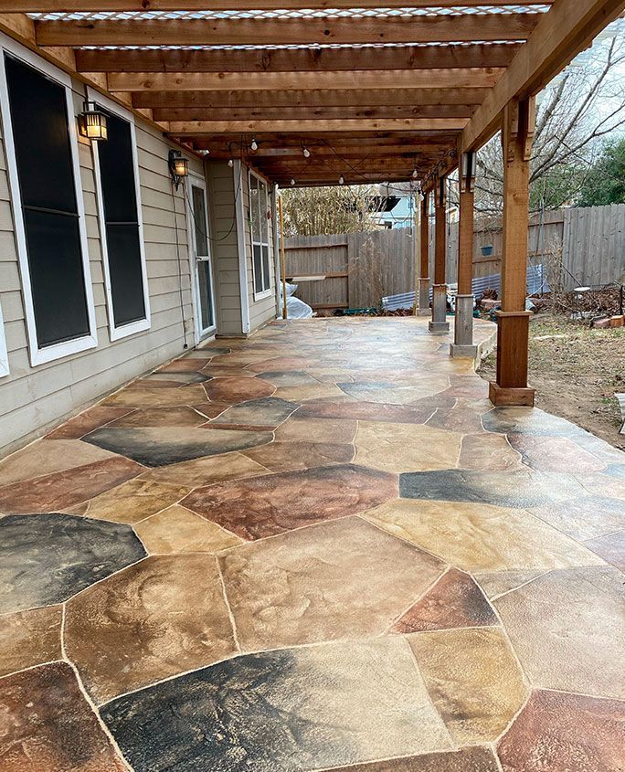 Patio with flagstone-patterned concrete floor under a wooden pergola, extending from a house.