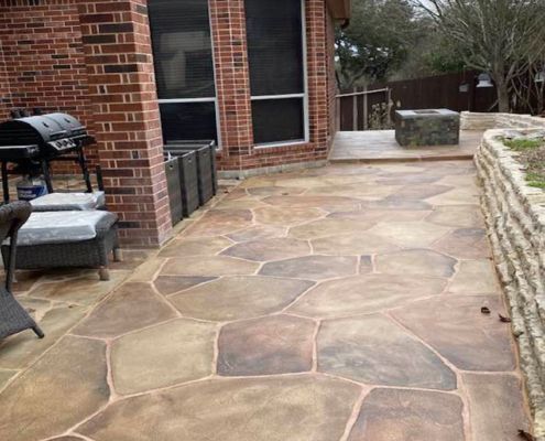 Stone-patterned concrete patio with a brick house and built-in fire pit.
