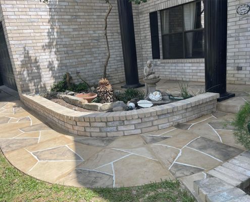 Stone pathway leading to a raised garden bed with a statue, next to a brick house.